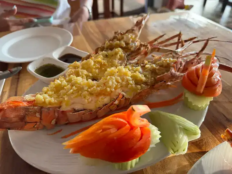 Two lobster halves topped with golden garlic, with carved tomato and cucumber and two dipping sauces
