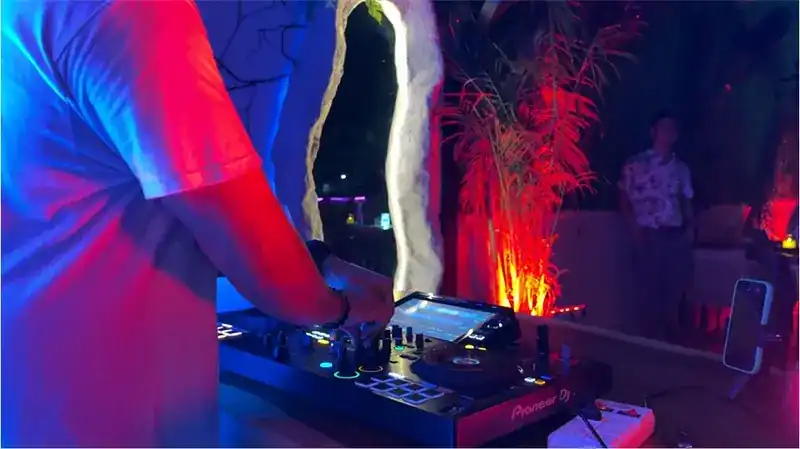 Hands on the DJ deck on the rooftop, palms lit red behind