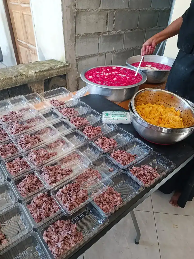 Purple rice packed into clear boxes beside bowls of red and yellow