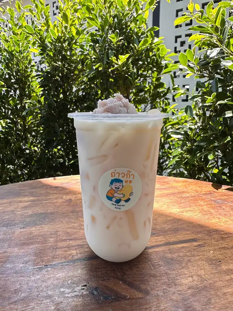 Iced soy milk with toppings in a cup with the Taoka sticker, on a table in the garden