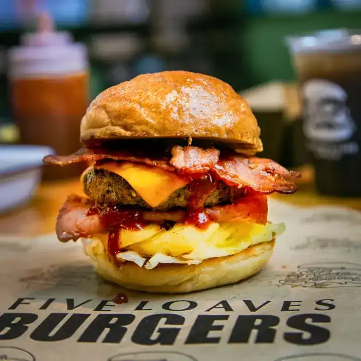 A Five Loaves burger with bacon, cheddar and sauce, on their printed burger paper
