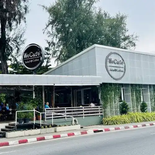 A grey café building with round We Cafe' signs, a terrace and a ramp at the front
