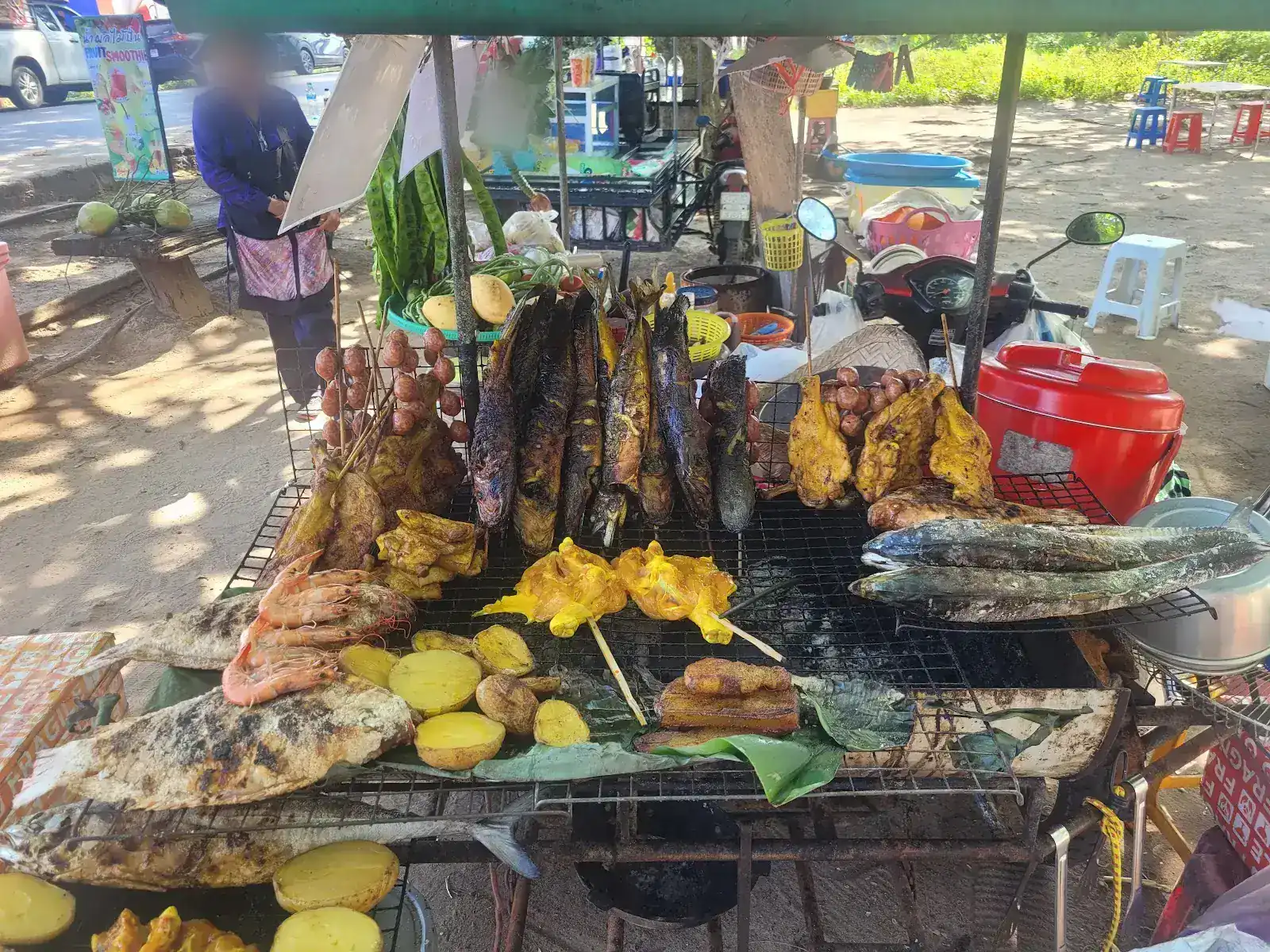 A street grill loaded with chicken on bamboo skewers, whole fish, prawns and sausages