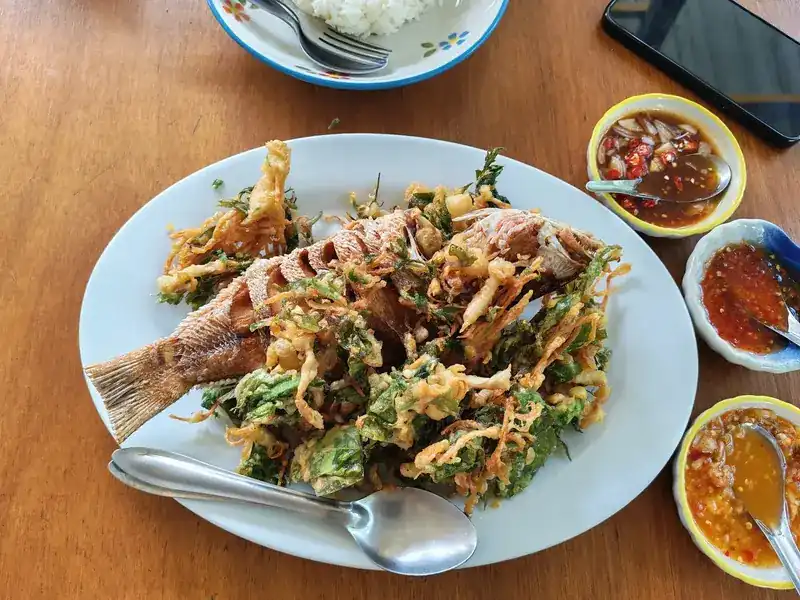 A whole fried fish under crisp-fried herbs, with three small bowls of dipping sauce