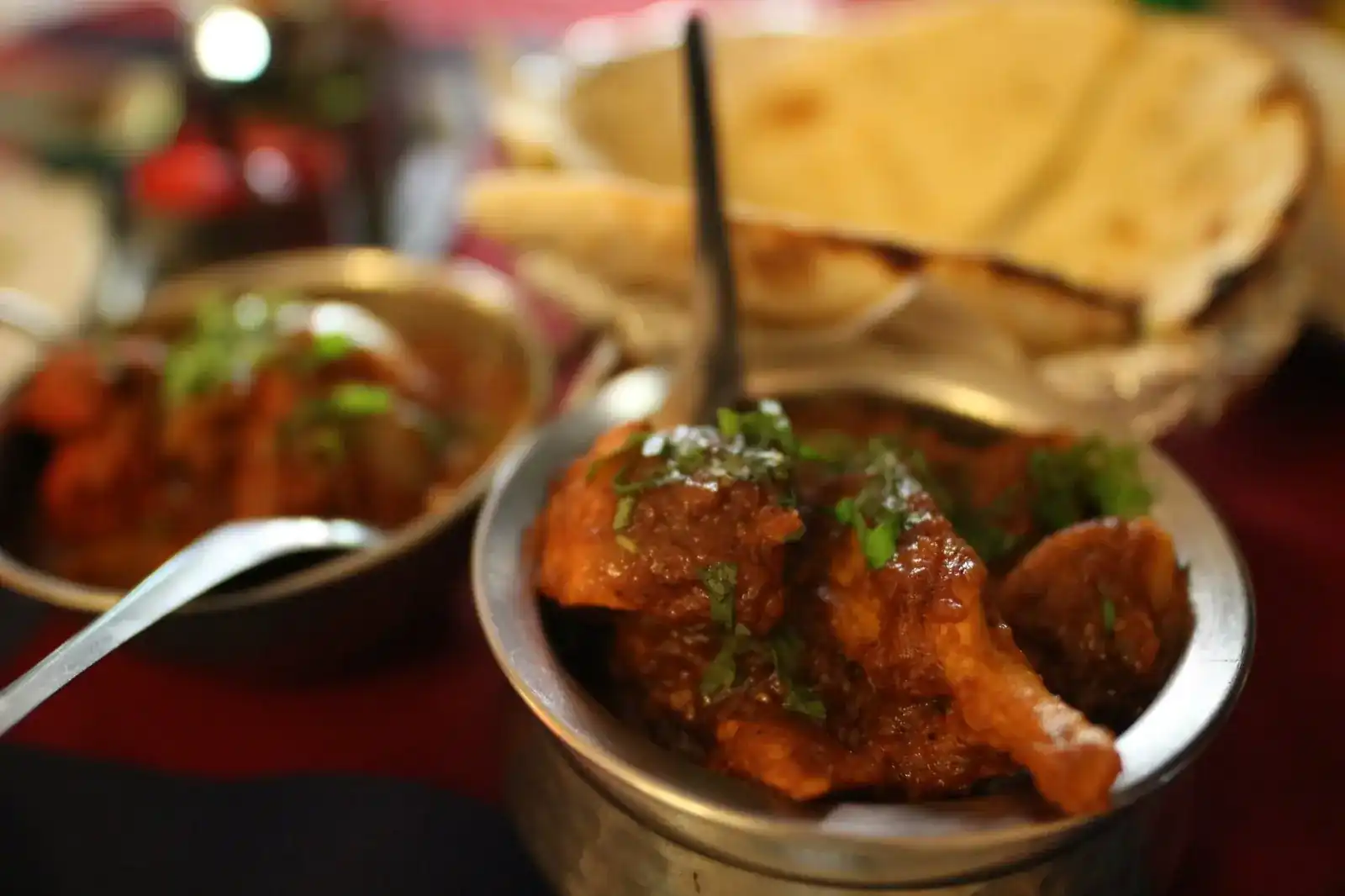 Chicken curry in a steel bowl with naan behind it