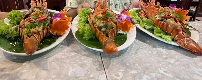 Three lobsters, split and topped, on plates with lettuce and orchids / ล็อบสเตอร์สามตัวผ่าครึ่งพร้อมเครื่อง จัดจานกับผักและกล้วยไม้