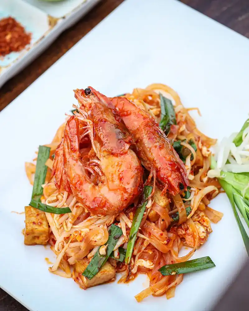 Pad thai with prawns, tofu and chives on a white plate