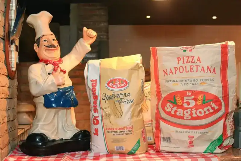 Sacks of pizza flour on a checked tablecloth beside a chef figurine