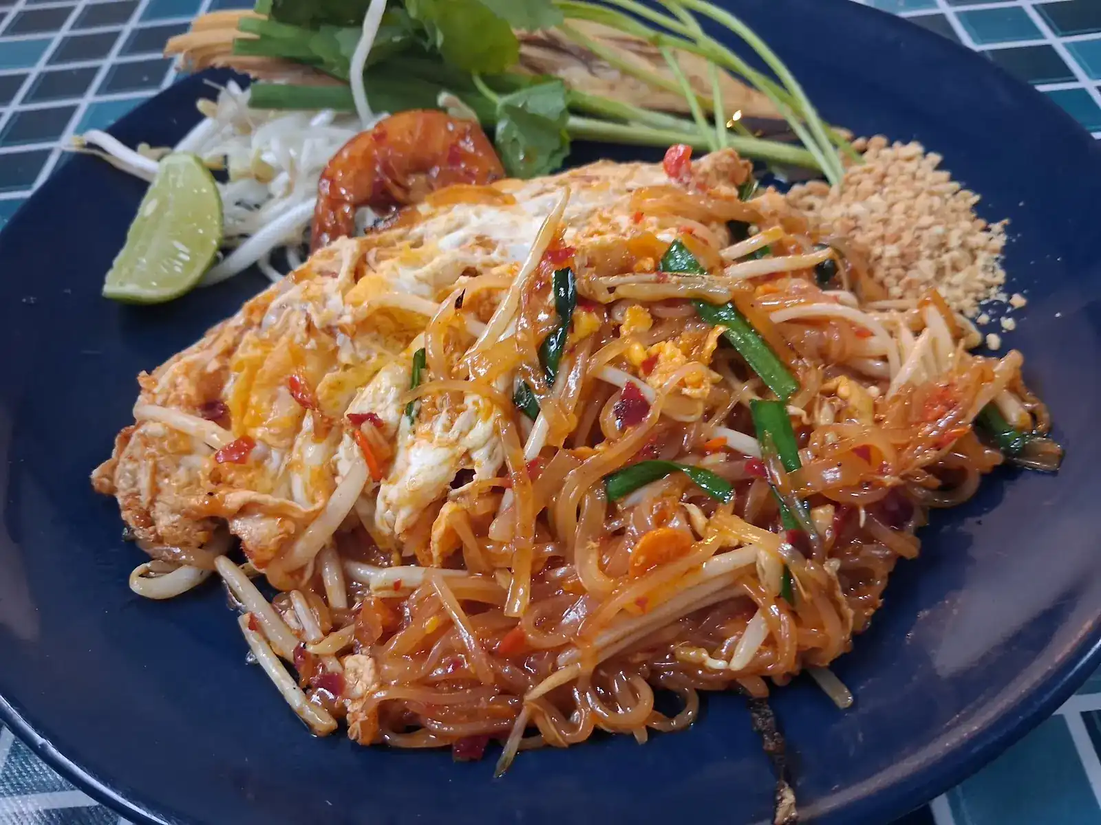 Pad Thai with shrimp, egg, crushed peanuts, lime and bean sprouts on a navy plate