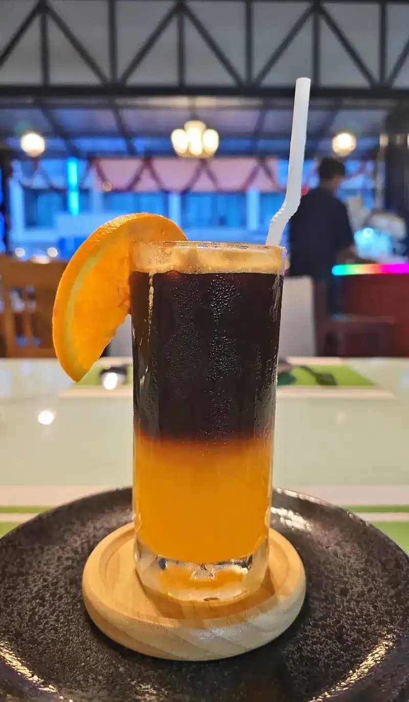 A layered iced drink, dark over orange, with an orange slice