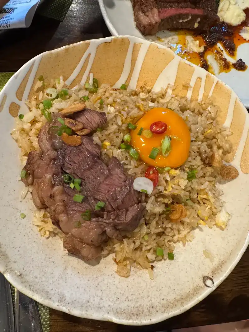 Fried rice with sliced beef and an egg yolk, a steak behind it