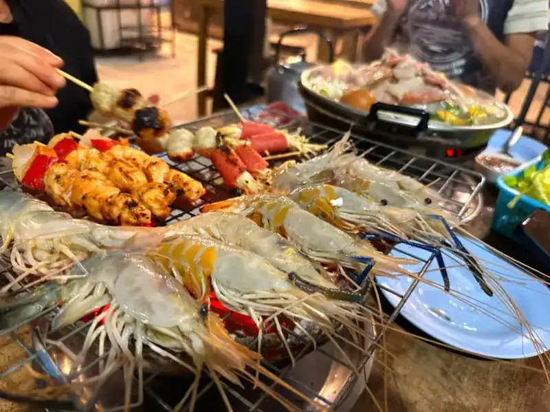 Skewers and whole prawns on the grill, with a moo kratha pan behind