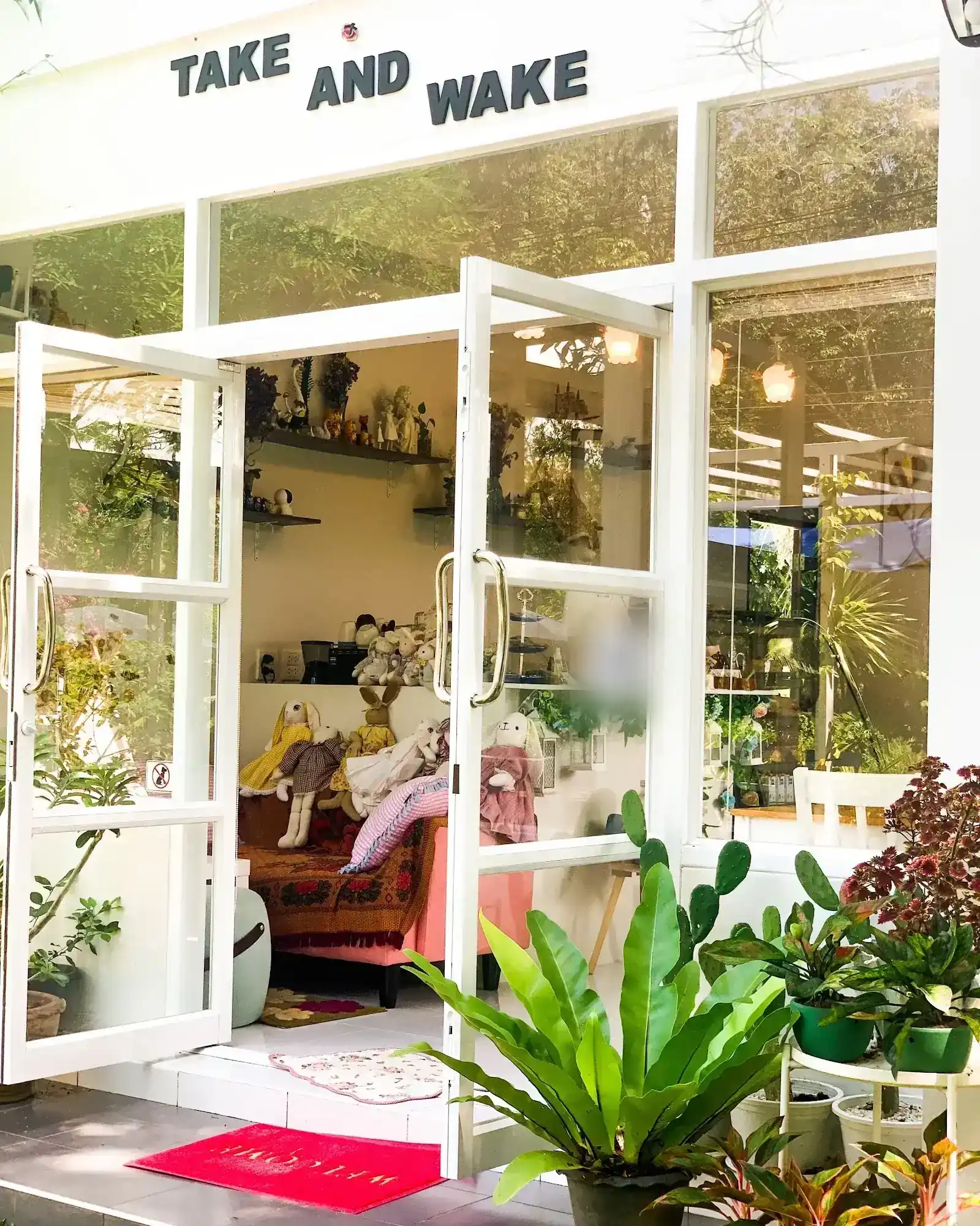 The white glass shopfront with its doors open: a sofa of rabbit dolls, shelves of ornaments and potted ferns at the step