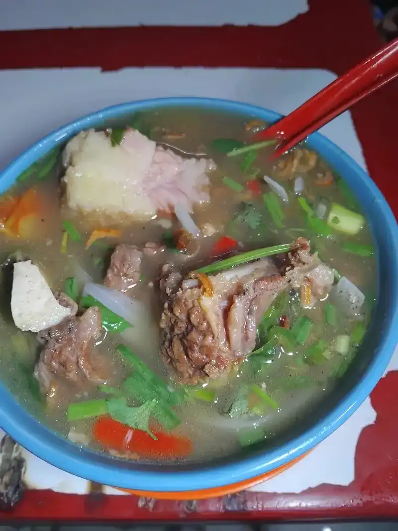 A blue bowl of clear soup with bone-in meat, herbs and chilli