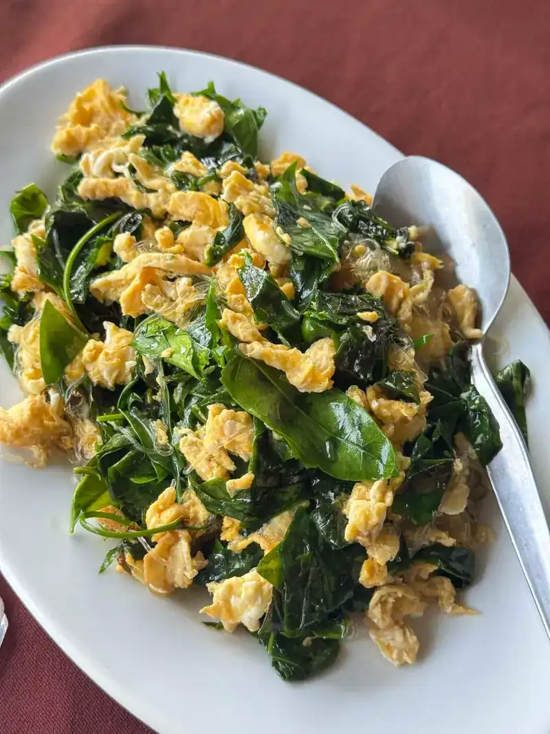 Green leaves stir-fried with egg on a maroon tablecloth