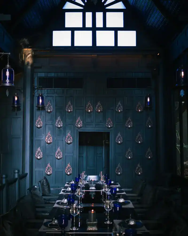 A long table set with cobalt glasses before a dark teal wall of carved flame motifs and blue lanterns