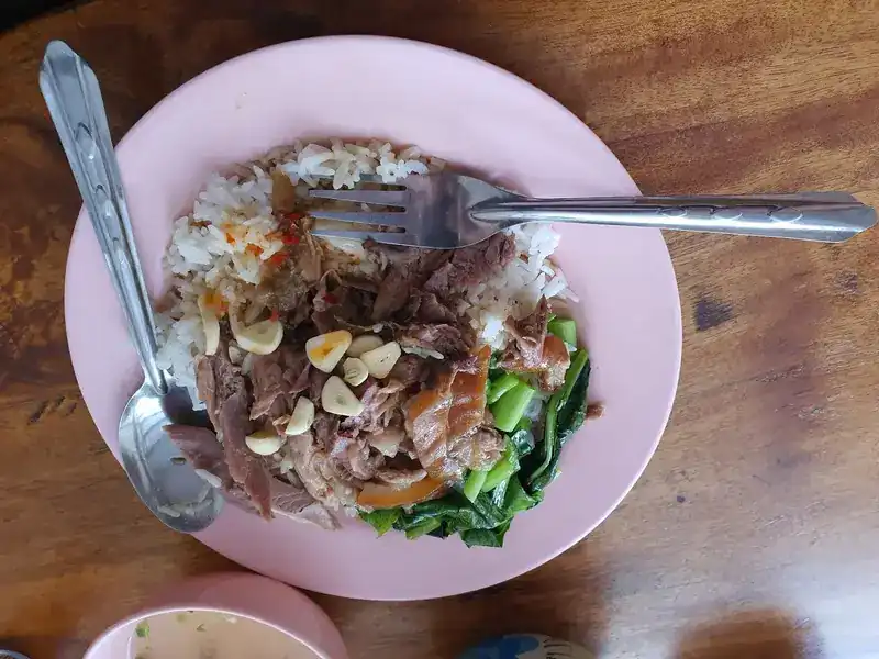 Pork leg on rice with garlic and chilli, a fork and spoon on a pink plate