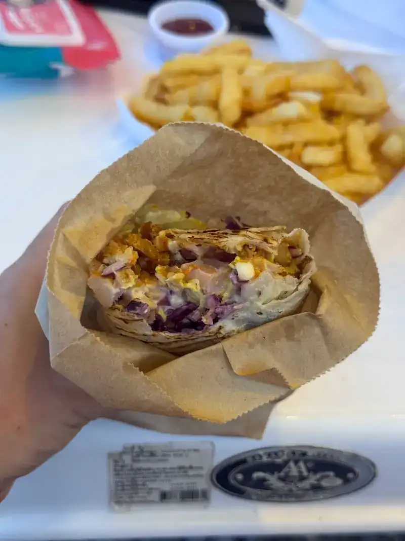 A shawarma held in a paper bag, cut open to show the filling, with fries behind