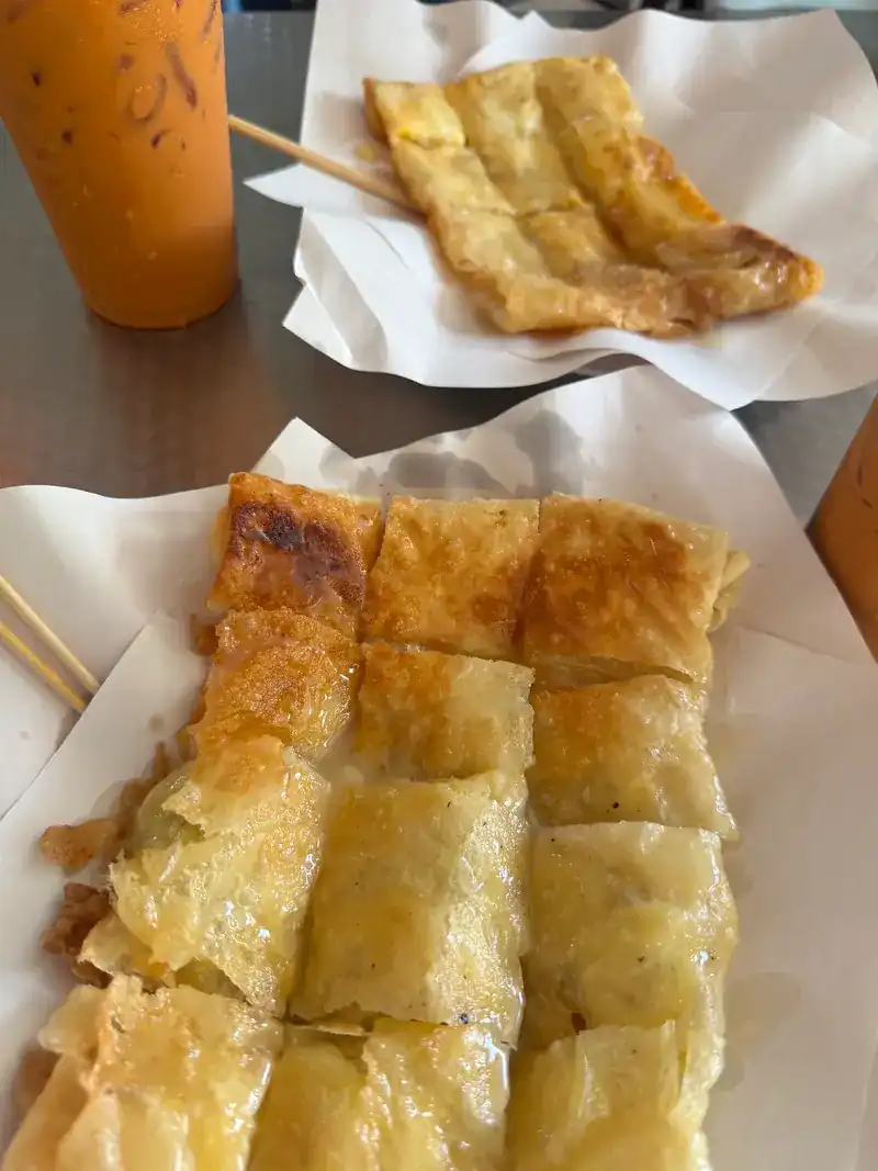 Roti cut into squares on white paper, with a cup of iced Thai tea