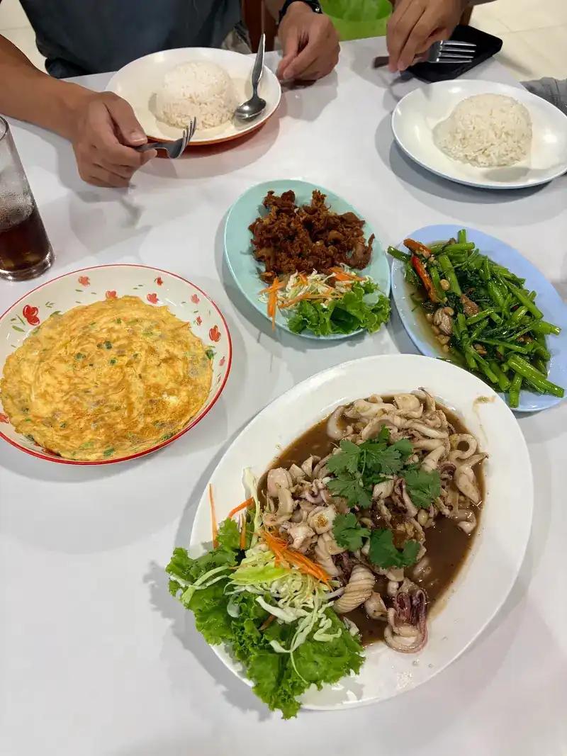A shared table seen from above: squid, an omelette, stir-fried greens, fried pork and plates of rice