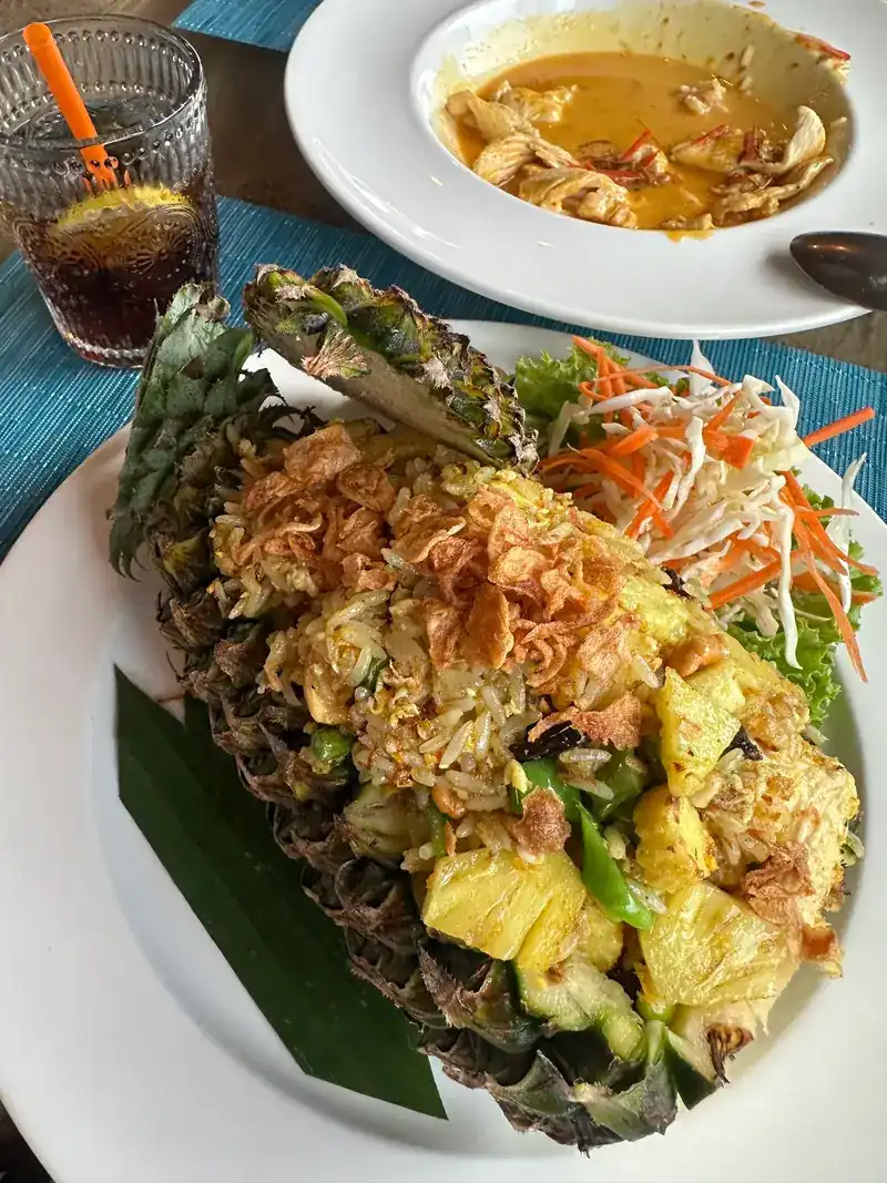 Fried rice served in a halved pineapple, topped with fried shallots