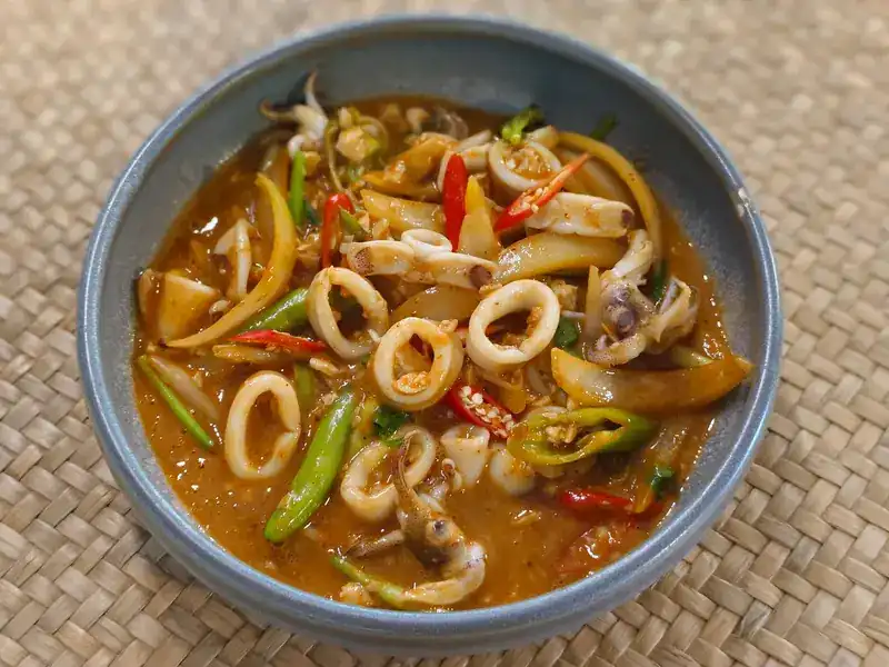 Squid with chillies, onion and long beans in a red sauce, in a grey bowl