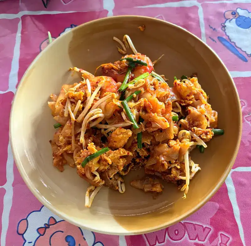 A bowl of shrimp pad thai on a pink cartoon tablecloth