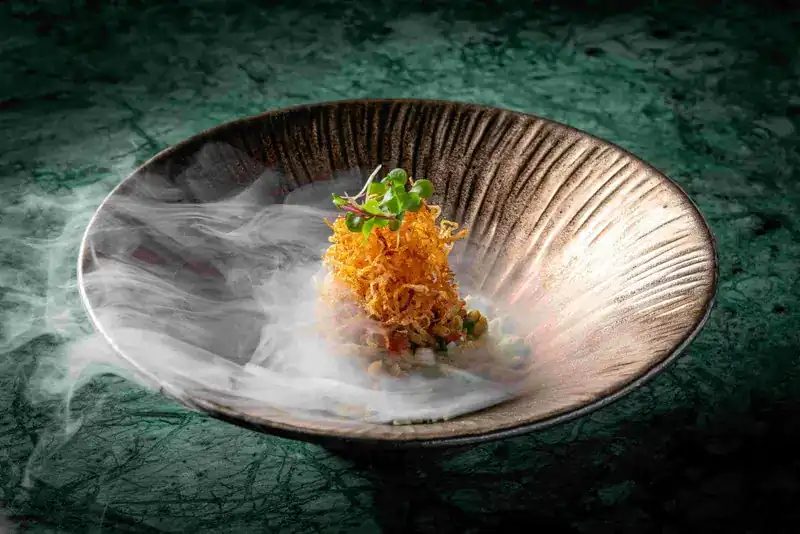 Puffed rice salad under crisp fried strands in a ribbed bowl, smoke drifting across it