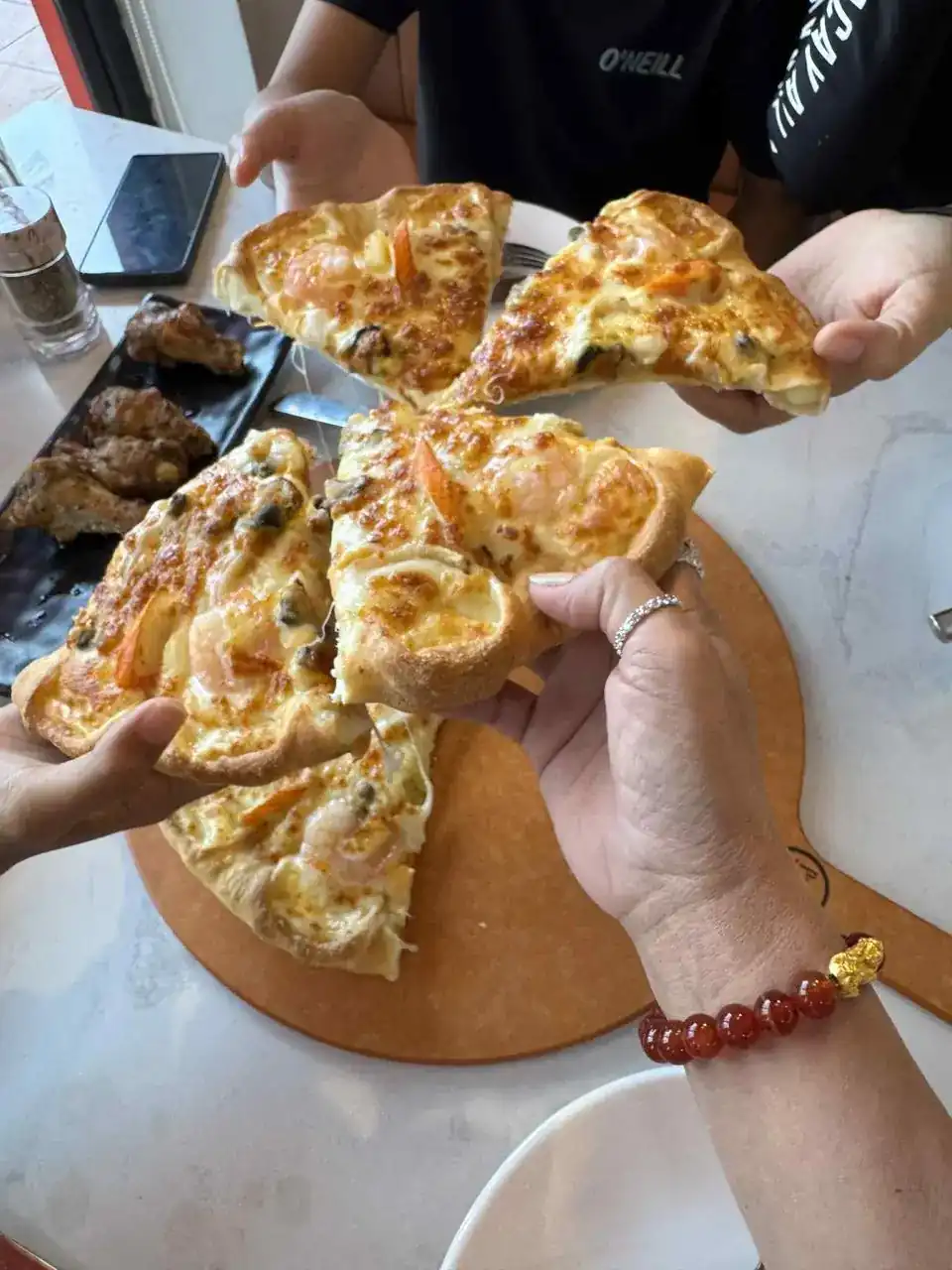 Hands pulling apart slices of a golden, cheese-topped flatbread over the table