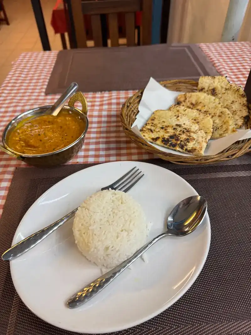 A table on red checks with rice, a curry and a basket of naan