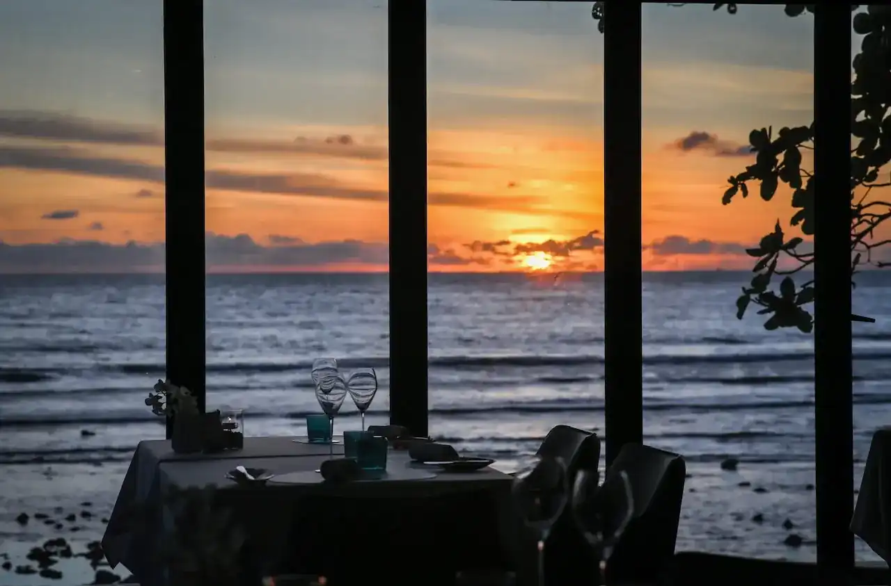 A set table in silhouette by the dining room windows, the sun going down over the Andaman Sea