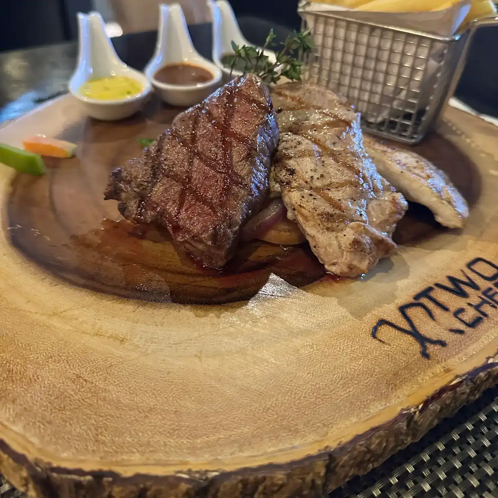 Grilled steaks on a wooden board branded Two Chefs, with fries and three sauces