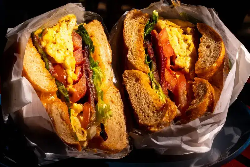 A bagel sandwich cut in half, with scrambled egg, bacon, tomato and lettuce, wrapped in paper