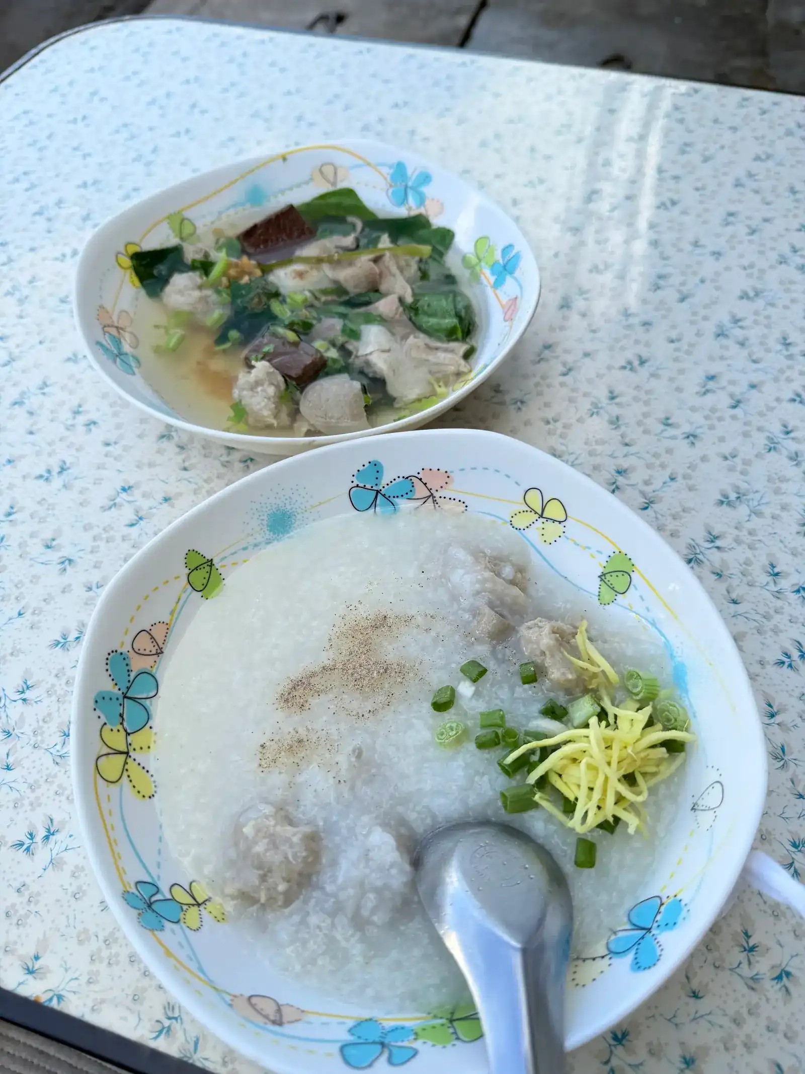 A bowl of rice porridge with pork balls, ginger and spring onion, and a bowl of clear soup with pork blood, pork balls and green leaves