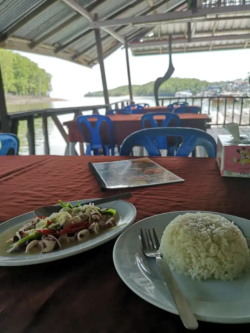 A table by the rail with a squid dish and rice, the water and green hills behind