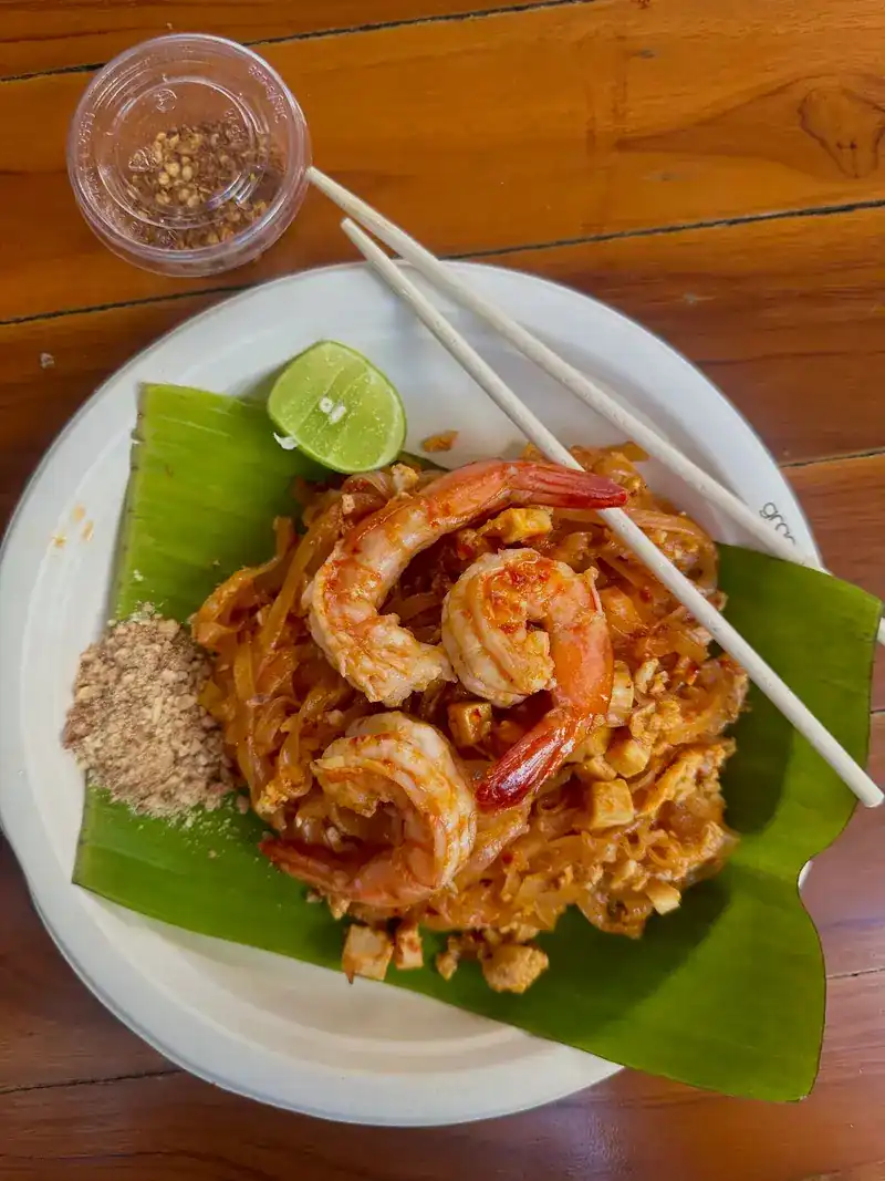 Pad thai with shrimp on a banana leaf, lime and crushed peanuts beside it