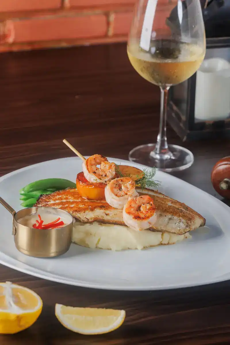 Grilled fish fillet topped with prawns on mashed potato