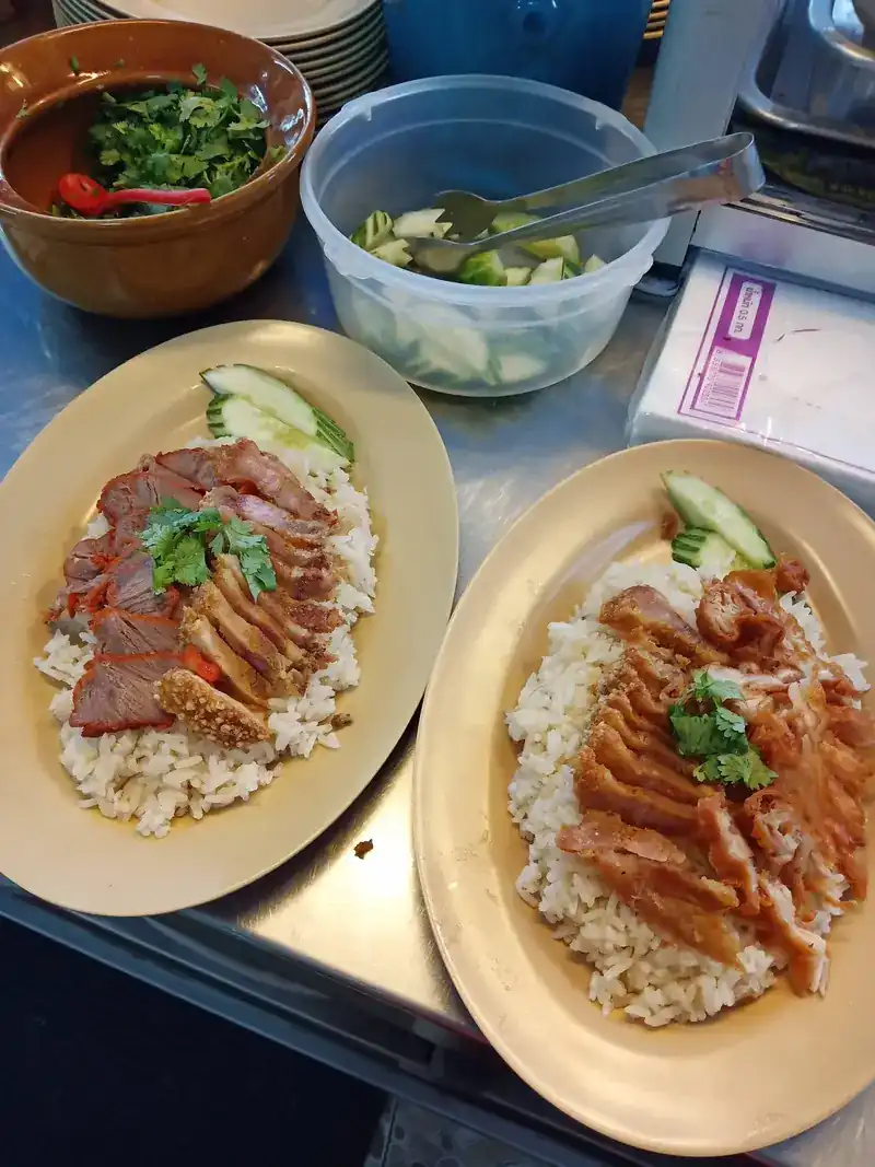 Two plates of pork on rice at the counter, beside bowls of coriander and cucumber
