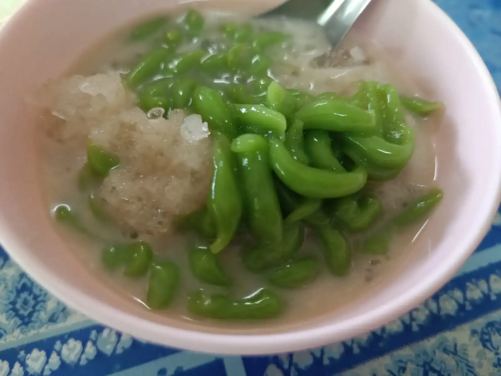 Green pandan lod chong in coconut milk with shaved ice, in a pink bowl