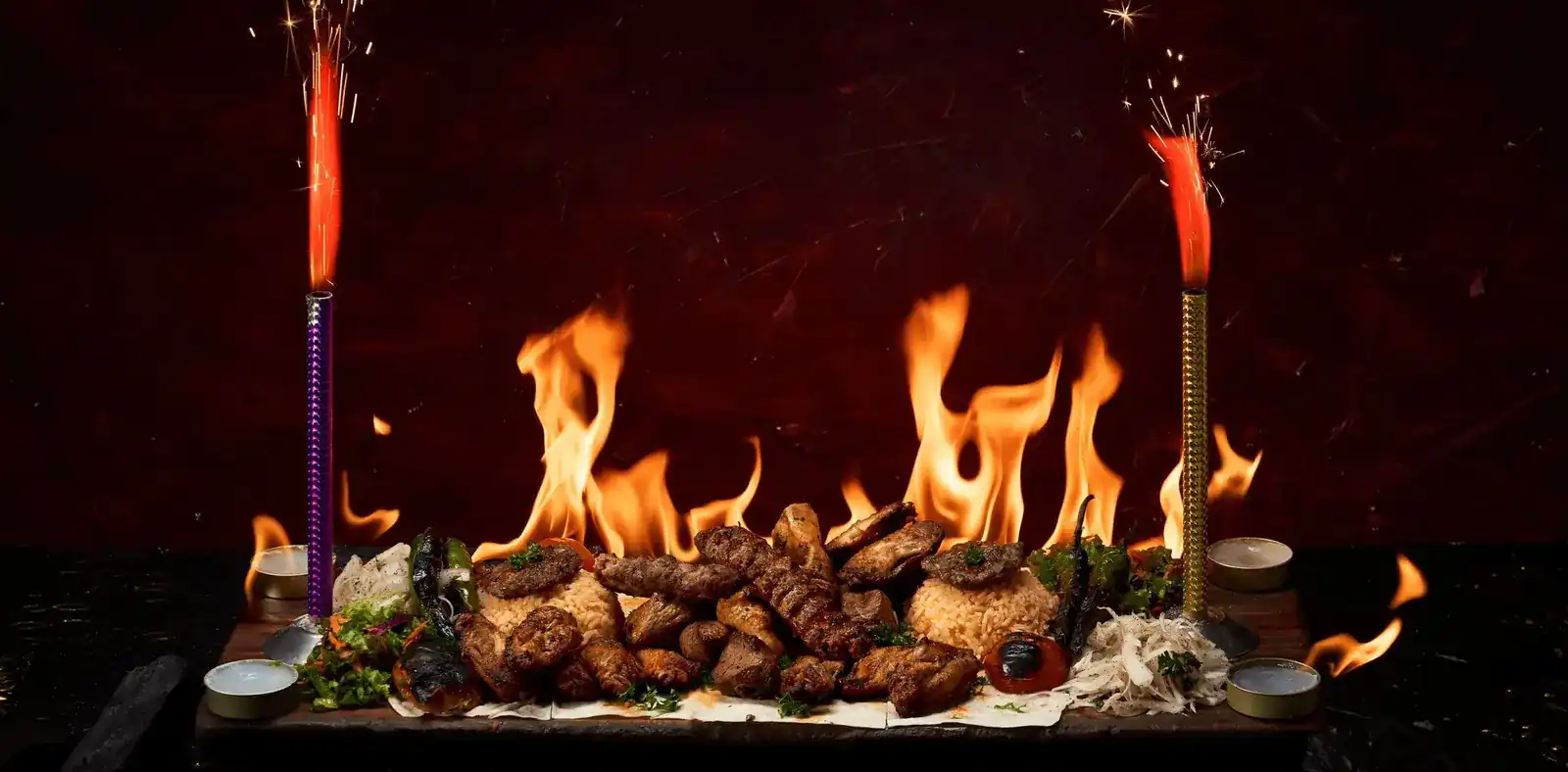 A long platter of grilled kebabs in flames between two sparklers