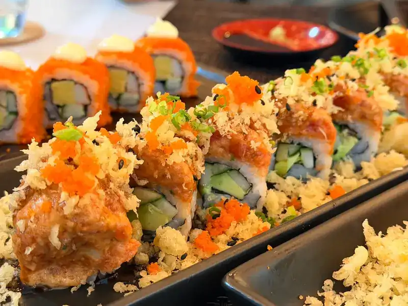 Sushi rolls topped with crispy tempura flakes and orange ebiko on long black plates