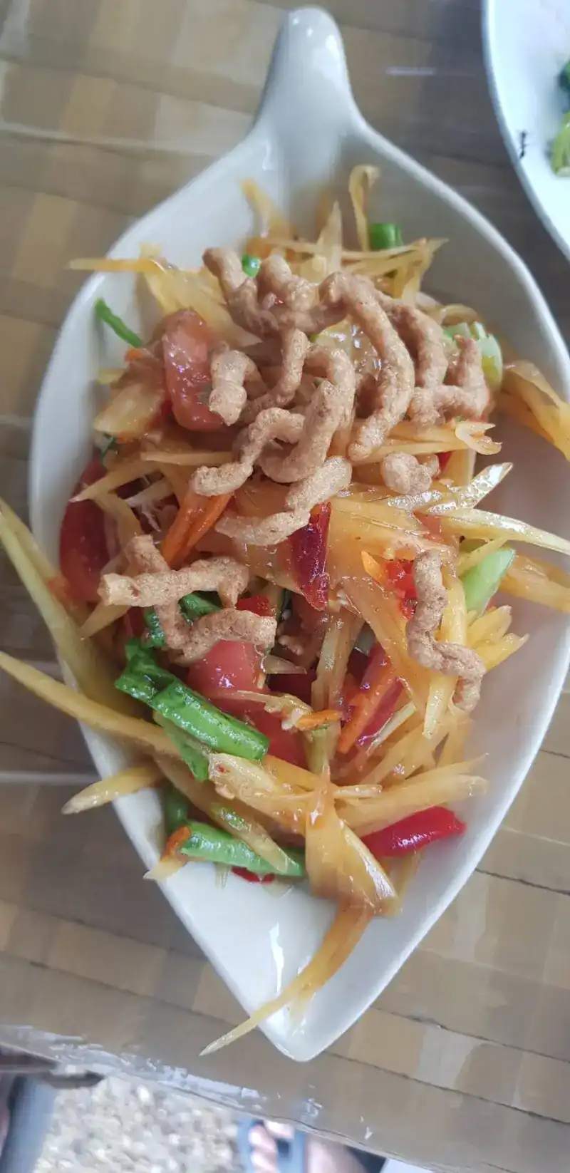 A spicy shredded salad with tomato, long beans and chilli under a crisp topping, on a leaf-shaped plate