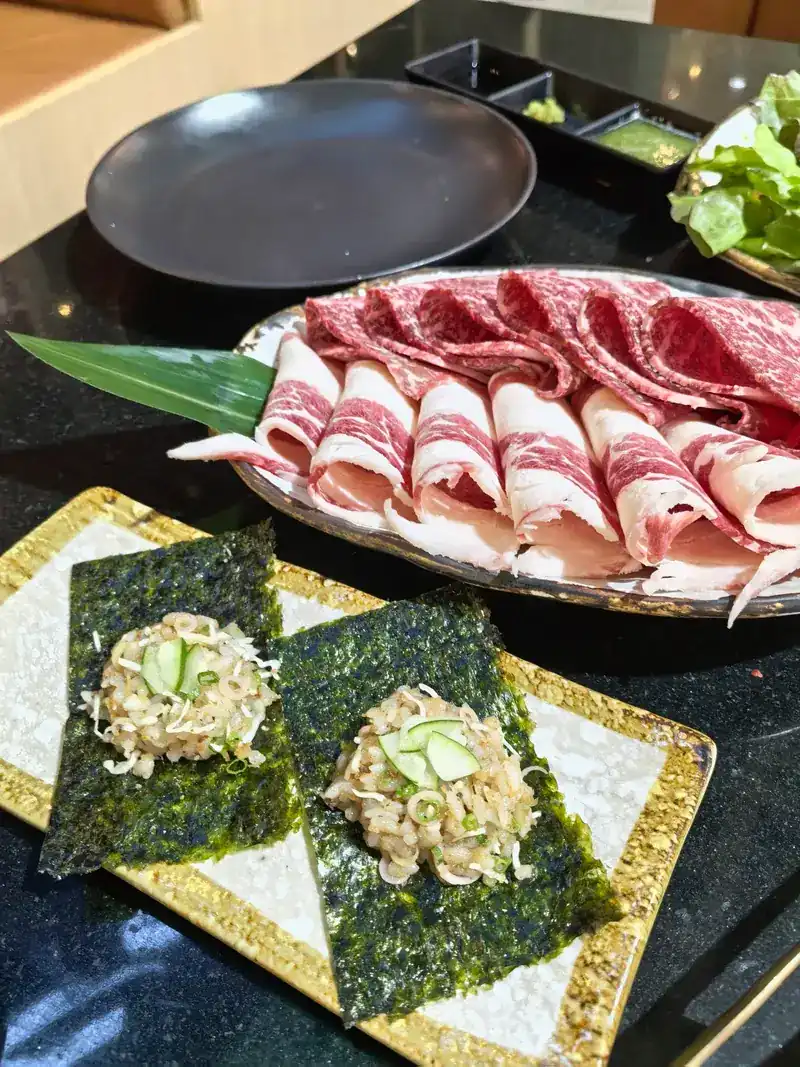 A plate of sliced wagyu beside two topped nori squares
