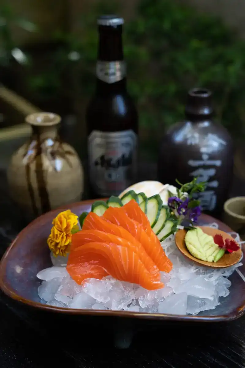 Salmon sashimi fanned out on ice with cucumber and flowers