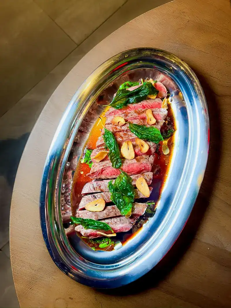 Sliced chargrilled beef with crisp basil leaves and garlic on a silver platter / เนื้อย่างถ่านหั่นชิ้นกับใบกะเพรากรอบและกระเทียมบนถาดเงิน