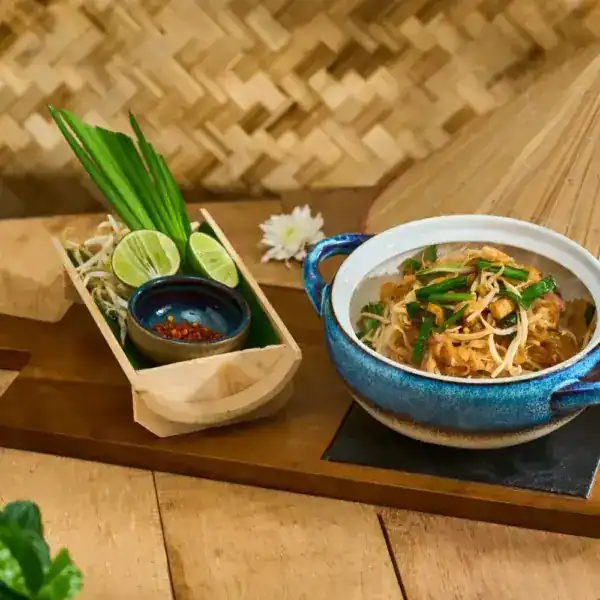 Pad Thai in a blue clay pot with lime and bean sprouts
