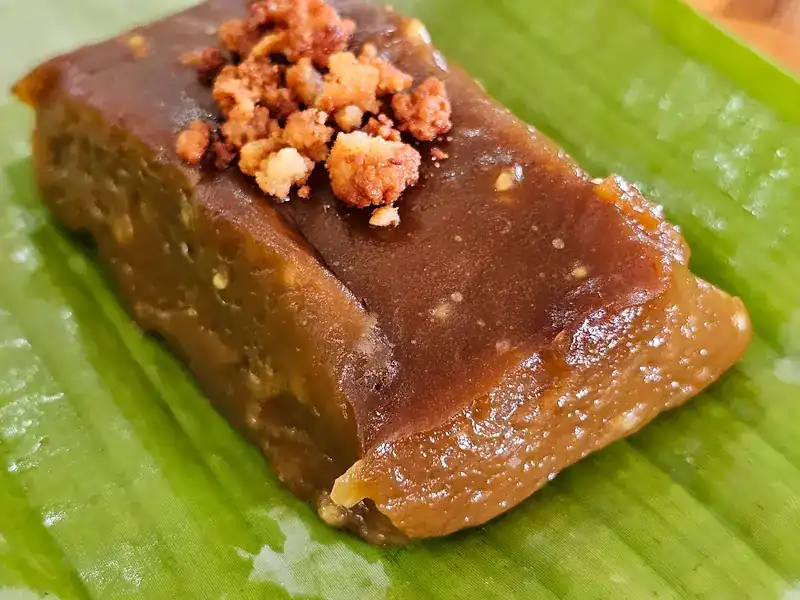 A dark-brown khanom with a crumbly topping, on banana leaf