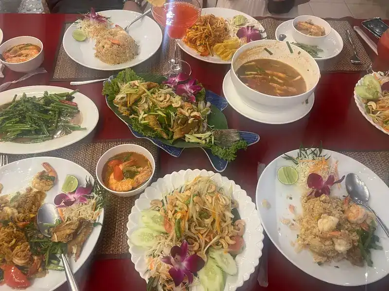 Pad thai, fried rice, tom yum and stir-fried greens spread over a red tablecloth / ผัดไทย ข้าวผัด ต้มยำ และผักผัดวางเต็มโต๊ะผ้าแดง