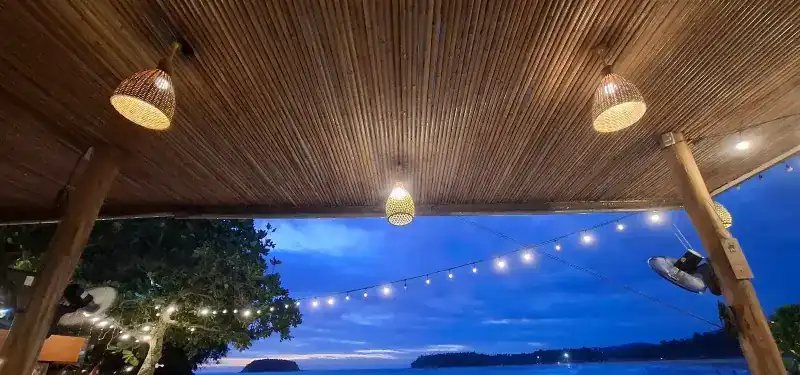 Woven lamps under the bamboo roof at blue hour, with the bay and the island beyond