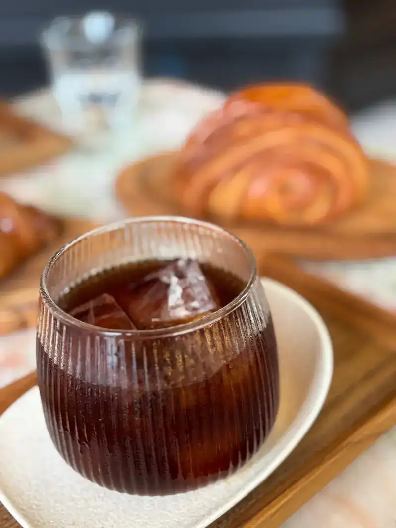 Iced black coffee in a ribbed glass, croissants behind it